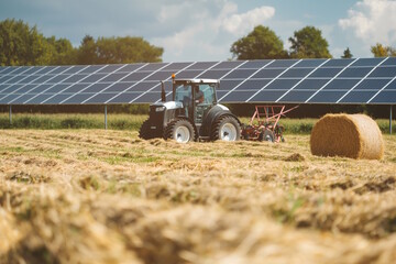 Tractor working in a field with solar panels in the background under a blue sky. Concept for...