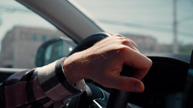 Close-up, a man in checkered shirt is driving a car. Close-up of a guy hand holding the steering wheel of a car.