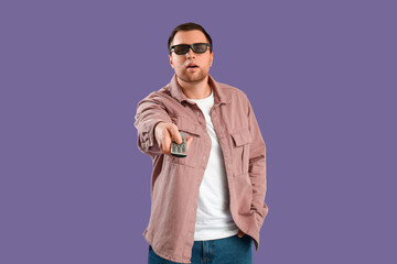 Fototapeta premium Happy young man with 3d eyeglasses and remote control on violet background