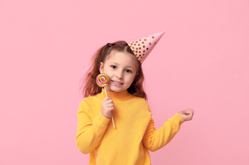 Cute little girl in holiday cap with lollipop on pink background