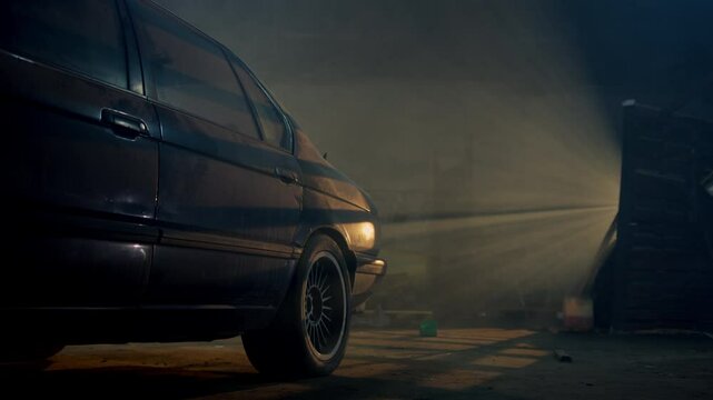 vintage youngtimer car, dusted with time, sits in a service station. The yellow glow from its window illuminates the interior, revealing its classic luxury.