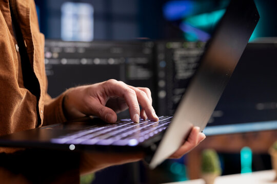 Computer scientist working from home using laptop, testing and deploying programs. Programmer checking code displayed on desktop PC screens in blurry background, close up shot