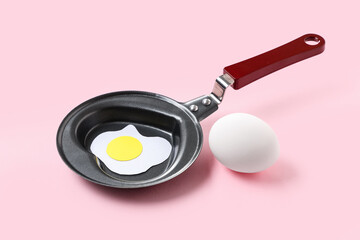Composition with egg, frying pan in shape of heart and fried egg on pink background