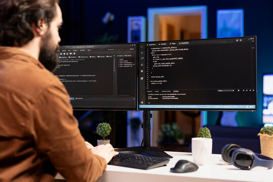 IT expert working from home developing software in JavaScript programming language using desktop PC. System engineer in living room writing lines of code on computer using keyboard