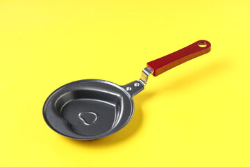 Heart-shaped frying pan on yellow background