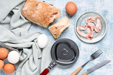 Composition with heart-shaped frying pan, napkin, cutlery and eggs on blue background