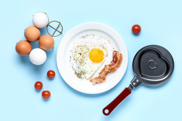 Composition with frying pan, heart-shaped fried egg and ingredients on blue background