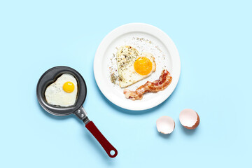 Composition with eggshell, heart-shaped fried egg in pan and in plate on blue background
