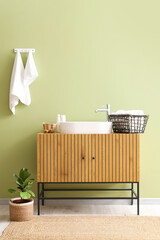 Clean towels on hooks and wooden chest of drawers with sink near green wall in bathroom