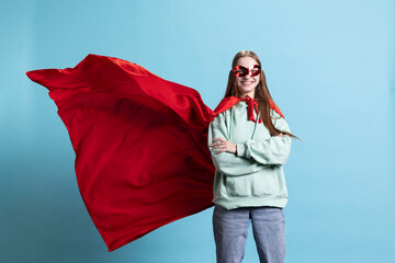Young girl wearing superhero costume and mask for Halloween, crossing arms, studio background. Portrait of woman dressed as comic book hero hiding identity, standing proud © DC Studio