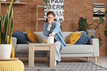 Obraz premium Sick young woman with tissue sand cup of hot tea coughing at home