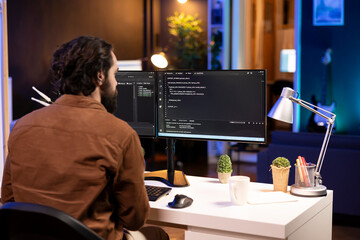 Computer operator doing software debugging on PC at home, checking broken lines of code displayed on monitors. IT expert in apartment fixing coding problems, typing on keyboard