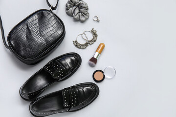 Stylish black loafers, bag, scrunchy, earrings, rings, brush and sculptor on grey background