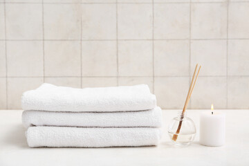 Beautiful composition with stack of clean soft towels, candle and aroma sticks in bathroom