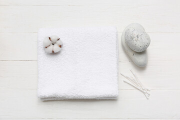 Beautiful composition with clean soft towel, cotton buds and spa stones on white wooden background