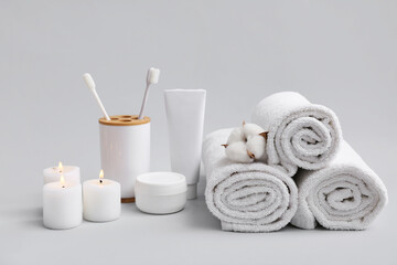 Composition with clean soft towels, candles, oral care kit and cotton flower on grey background