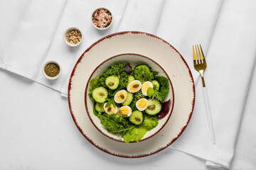 Bowl of healthy green salad with quail eggs, cucumber and pumpkin seeds on white background