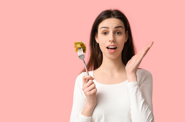 Surprised young woman holding fork with tasty ravioli on pink background