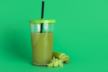 Glass of fresh juice with celery on green background