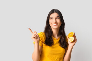 Beautiful young woman with citrus fruits pointing at something on grey background