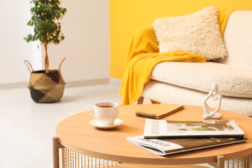 Cozy sofa with plaid and cushion, coffee table with cup of tea, human figure and magazine near orange wall
