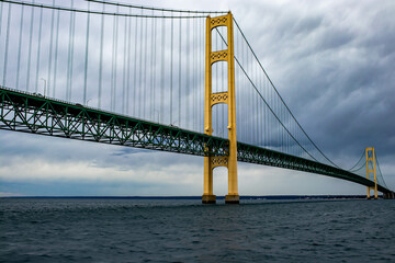 Mackinac Bridge with yellow towers and green truss structure spanning over Lake Michigan under a cloudy sky, captured during a road trip through Michigan.