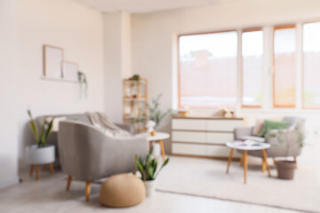 Armchairs with cushions, coffee tables and chest of drawers in interior of living room. Blurred view