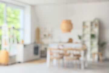 Blurred view of light kitchen with dining table, counters and shelf units