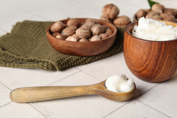 Bowl and spoon of shea butter with nuts on white tile background