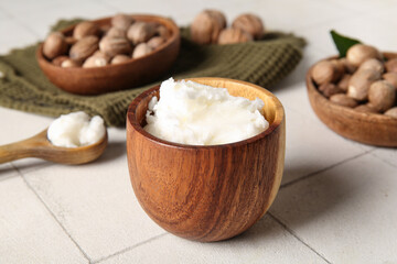 Bowl and spoon of shea butter with nuts on white tile background