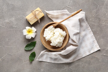 Bowl of shea butter with soap bar and plumeria flower on grey background