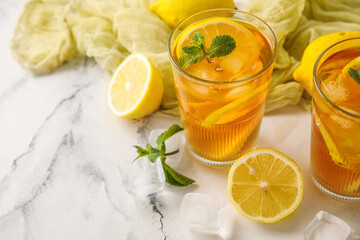 Lemons, ice cubes and glasses of tasty cold ice tea on marble background, closeup