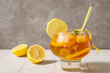 Beautiful glass of tasty cold ice tea and lemons on tile near grunge wall