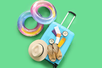 Inflatable rings, suitcase with flip-flops, sunscreen cream and passport with ticket on green background.. Travel concept. Top view