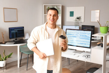 Handsome programmer with laptop and coffee cup in office