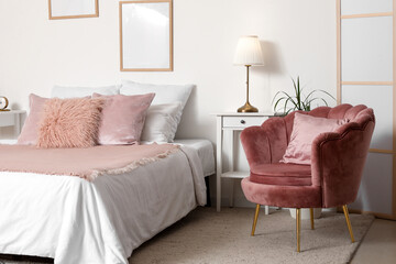 Stylish bedroom with comfortable bed, soft armchair and picture frames on white wall