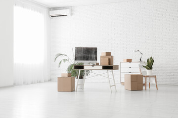 Workplace with wrapped computer monitor and cardboard boxes in office on moving day