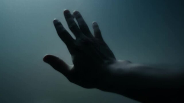 A hand frantically reaching out grasping for soing solid as the person stumbles over unseen obstacles in the darkness.