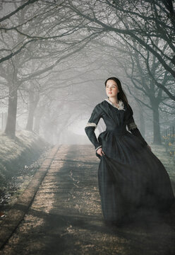 Young Victorian woman walking alone on a misty road with bare trees