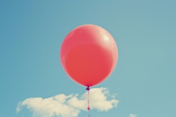 A lone red balloon floats in the air against a bright blue sky, ideal for use in illustrations about freedom, joy, or adventure