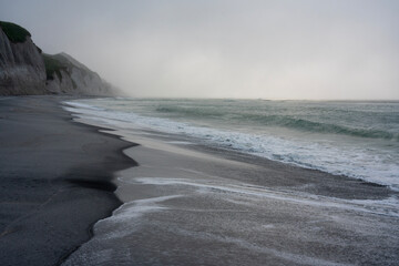 Cloudy stormy sunset, waves rolling on black sand, White Rocks, Iturup island, Far East