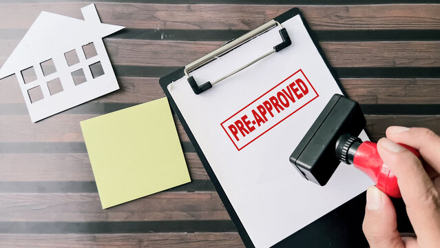Red Handle Rubber Stamper and Pre-Approved text above paperwork isolated on wooden background