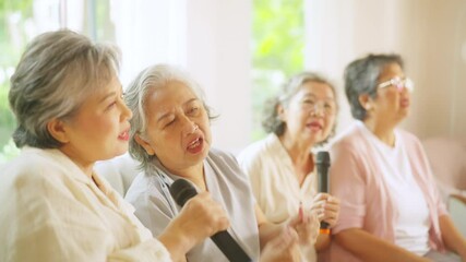 Group of Happy Asian senior women friends singing karaoke with dancing together in living room. Elderly retired people enjoy and fun indoor lifestyle spending time together with home entertainment.