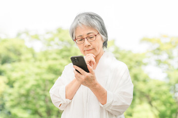 公園でスマホを使う高齢者女性（アプリ・操作・検索・写真・カメラ）
