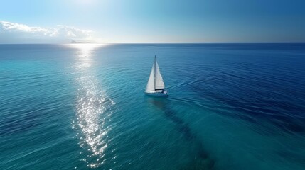 Obraz premium Aerial view of a sailboat navigating tranquil turquoise waters towards the horizon under a clear blue sky with the sun shining brightly.