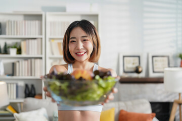 portrait attractive young woman in sportswear holding bowl of fresh vegetable standing in the living room after exercise,concept of healthy lifestyle,health care,vegetarian diet,loss weight