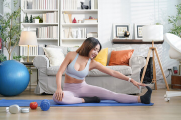 young attractive asian woman in sportswear sitting on yoga mat stretching legs before fitness training in the living room