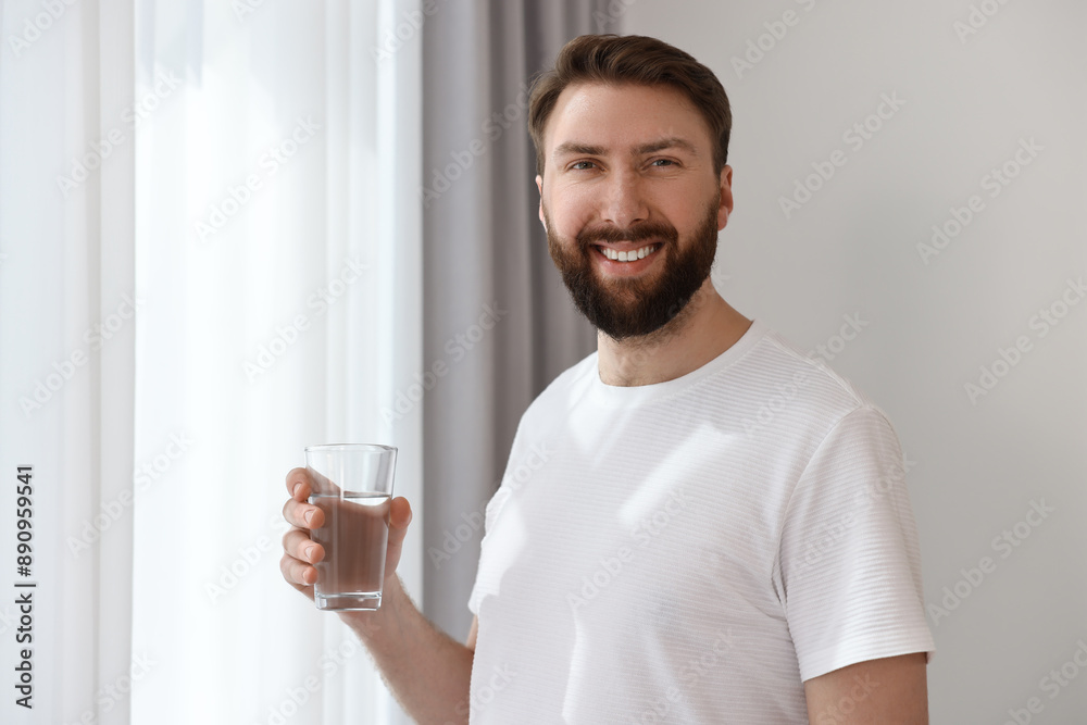 Sticker Happy young man with glass of water near window at morning