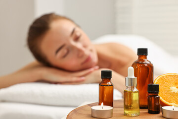 Fototapeta premium Aromatherapy. Woman relaxing on massage couch in spa salon, focus on bottles of essential oils, orange and burning candles