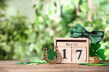 Composition with block calendar on wooden table against blurred greenery, space for text. St. Patrick's Day celebration